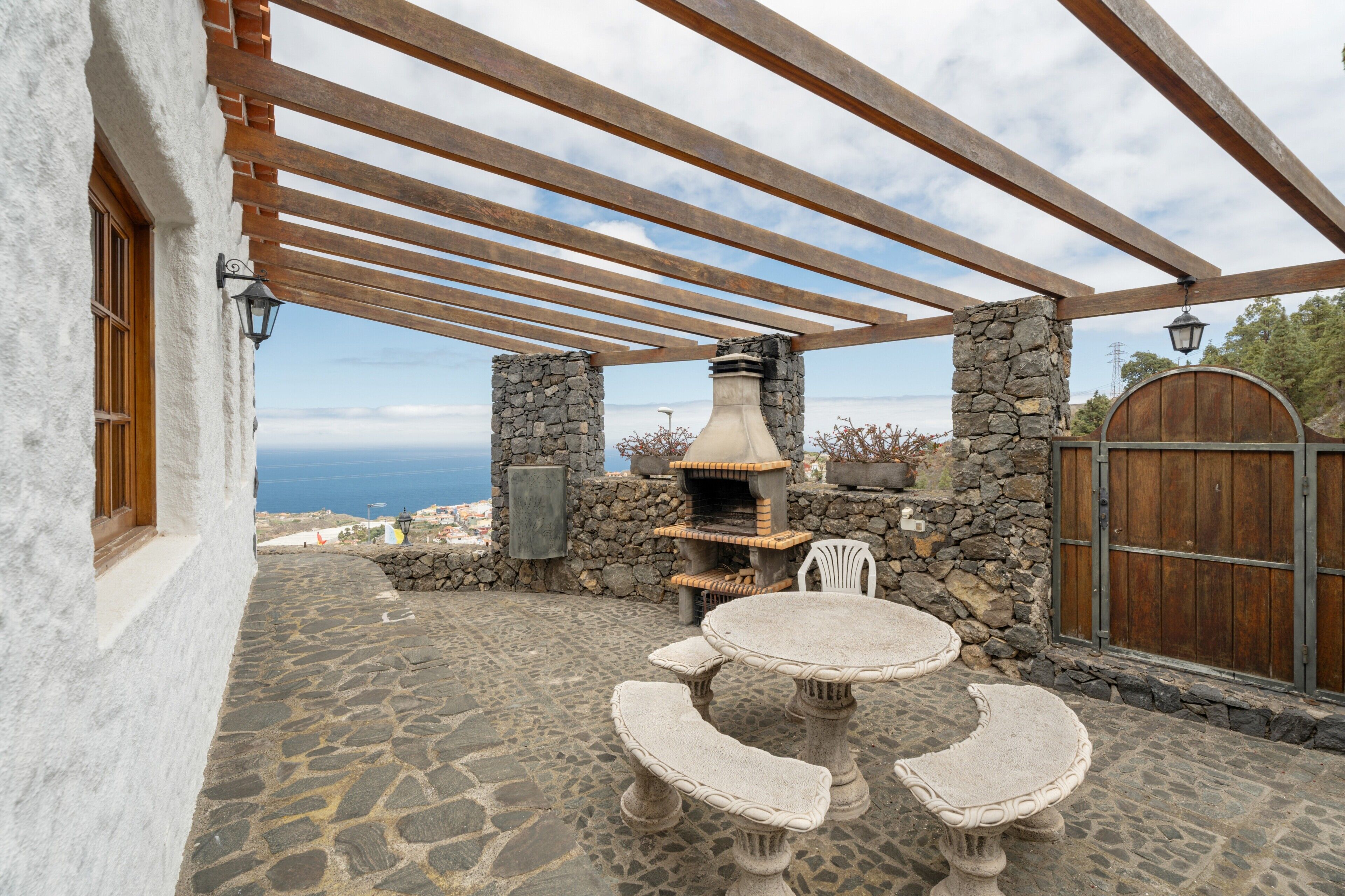 An outdoor patio with stone flooring, a stone chimney, and a wooden pergola.