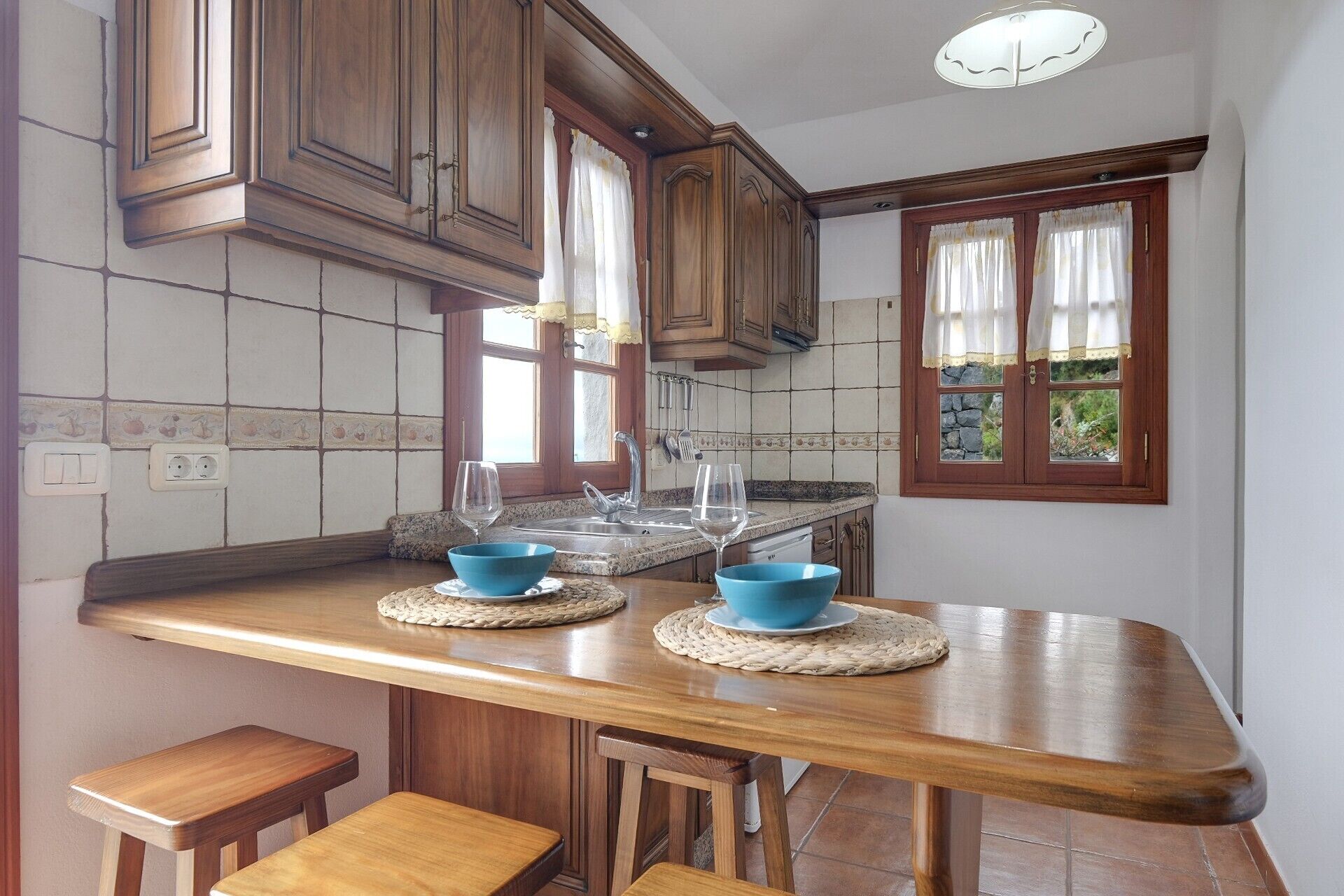 Een keuken met houten kastjes, een granieten aanrecht en een raam met gordijnen.
