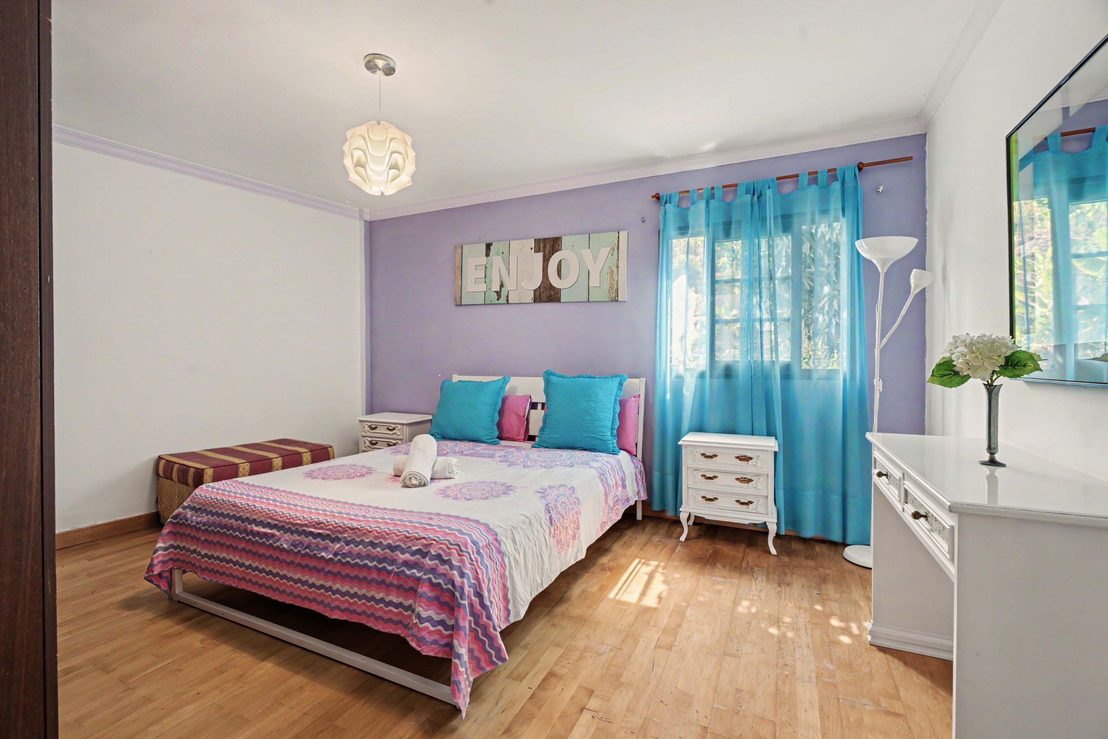 Une chambre à coucher comprenant un lit, des tables de chevet, une commode, un miroir et un panneau décoratif fixé au mur.