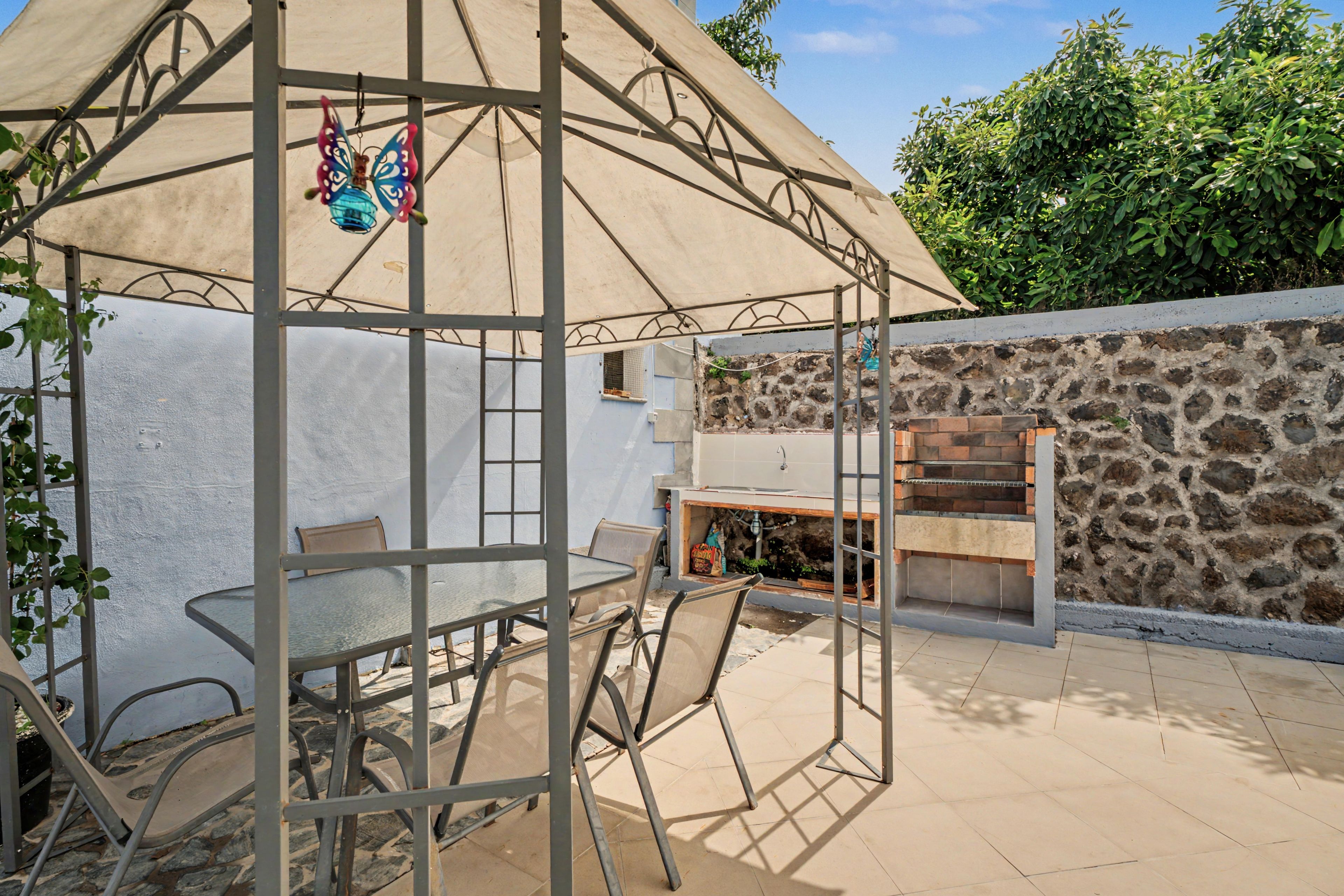 Un patio al aire libre con una mesa, sillas, una parrilla y un muro de piedra.