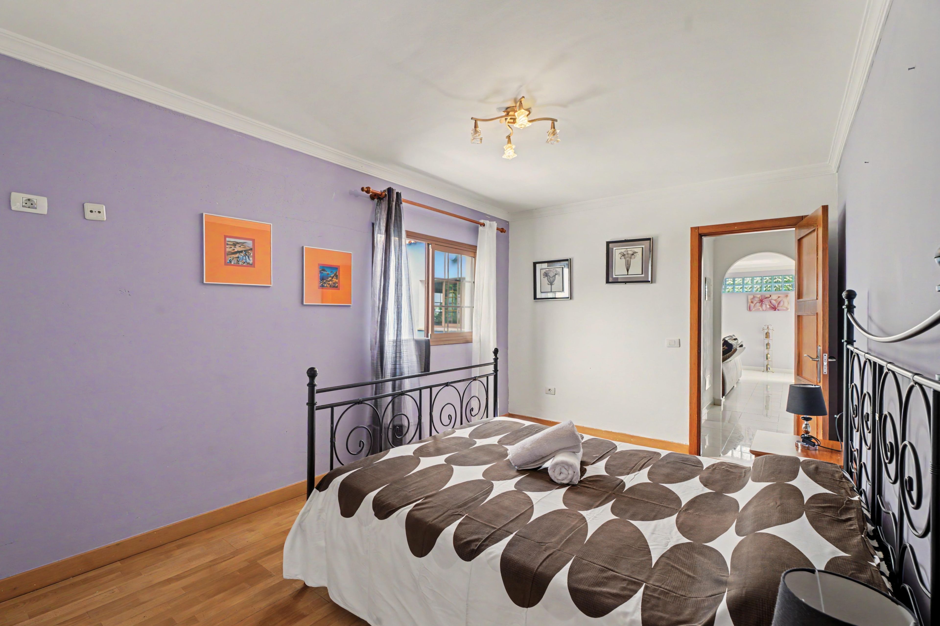 A bedroom with a bed, a window with curtains, and a door leading to another room.