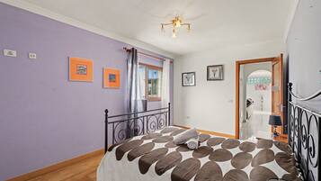A bedroom with a bed, a window with curtains, and a door leading to another room.