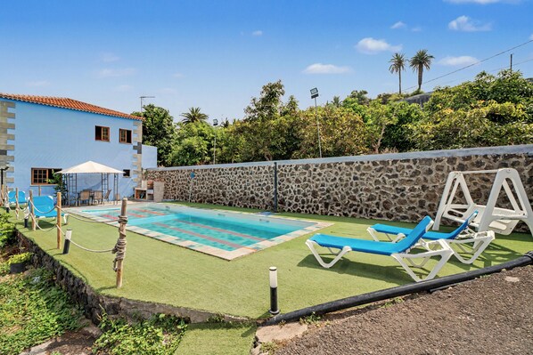 A pool area with a stone wall, lounge chairs, and a building with a blue facade.