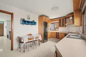 A modern kitchen with wooden cabinets, a stainless steel refrigerator, and a dining area with a table and chairs. - Holiday Home “Casa las Cañas” with Mountain View, Sea View, Pool and Terrace (Icod de Los Vinos)