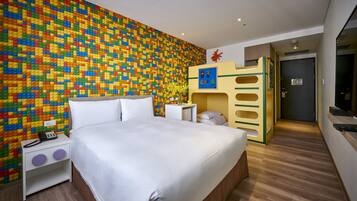 A bedroom with a colorful LEGO wall, a bed, a nightstand, and a small desk with a vase of flowers.