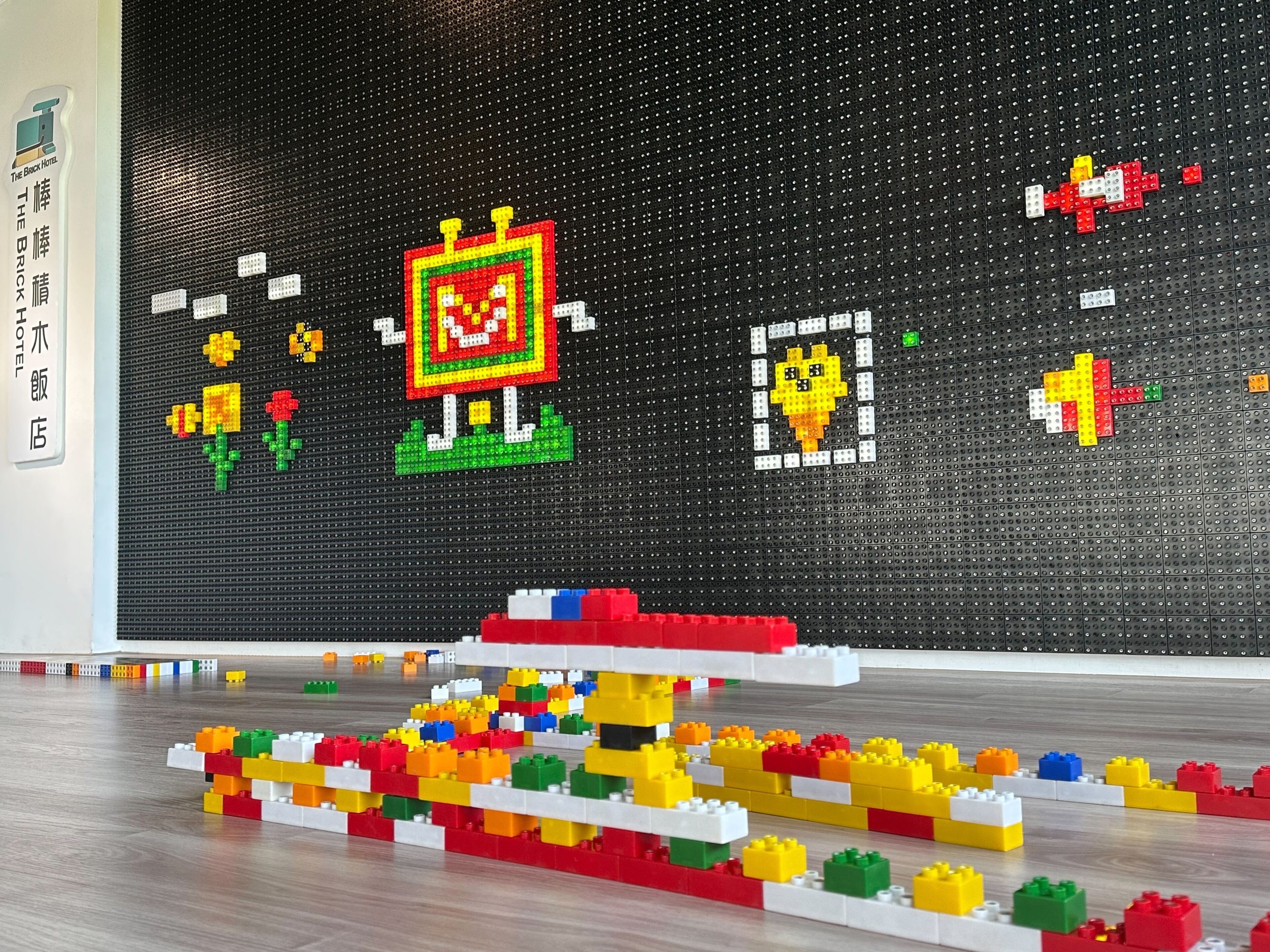 Un'esposizione in pixel art con il cartello di un albergo e un colorato allestimento LEGO sul pavimento.