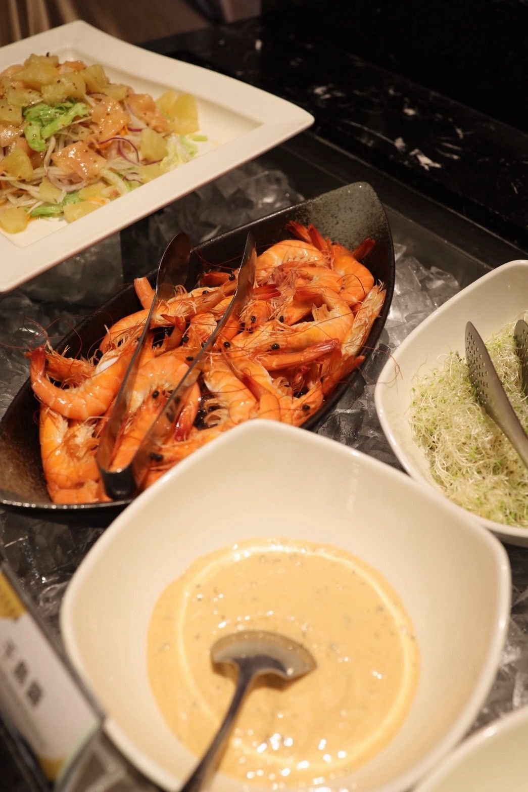 A kitchen counter with a pan of cooked shrimp, a bowl of sauce, and a plate of food.
