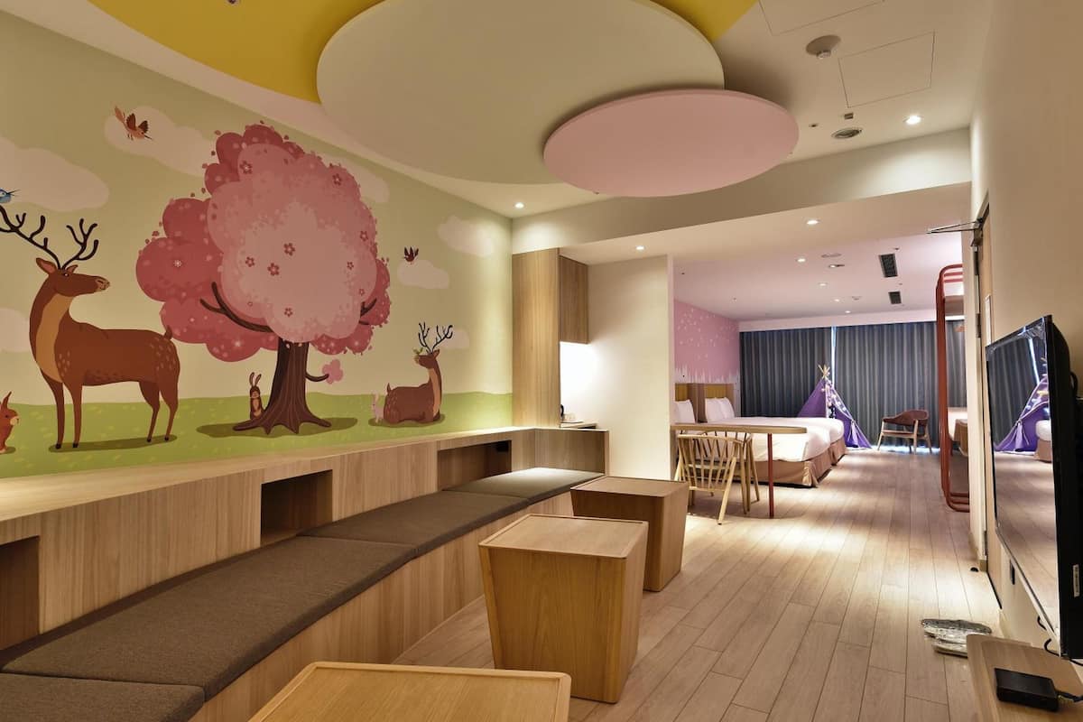 A modern hotel room with a large bed, a desk, and a seating area with a mural of deer and trees.