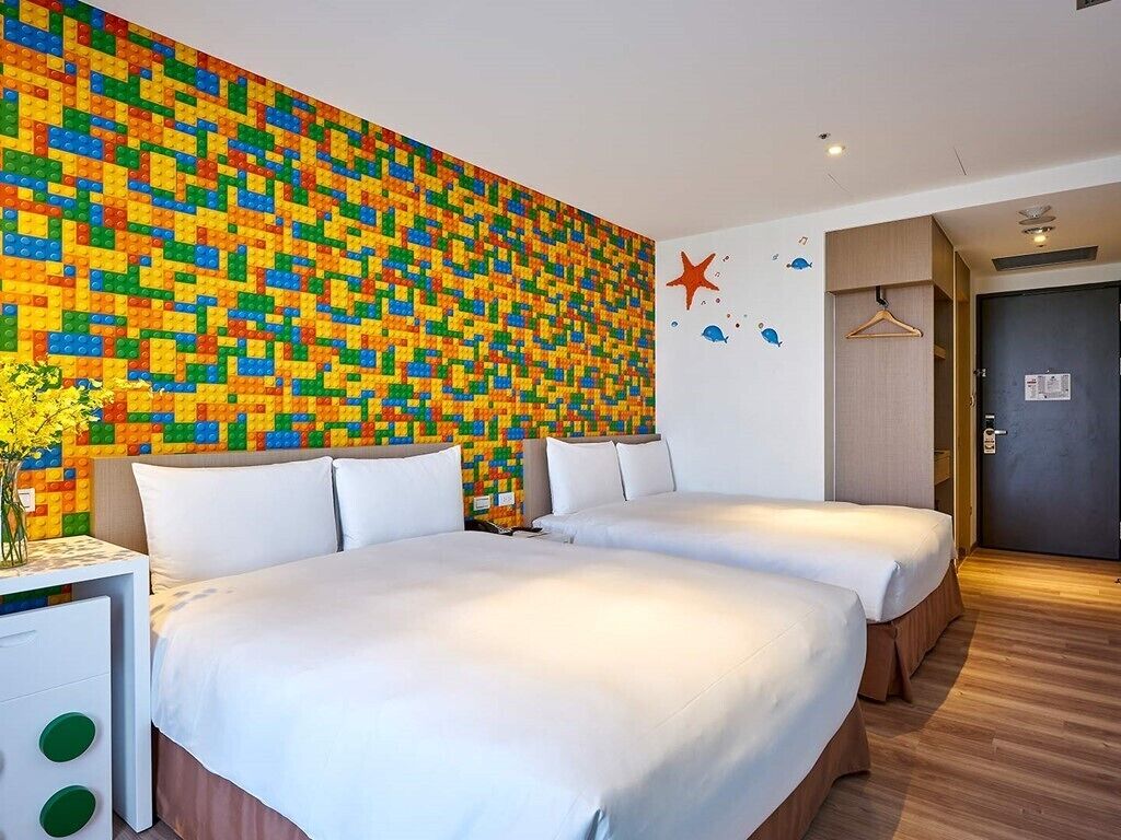 Une chambre d’hôtel avec deux lits, une mosaïque colorée au mur, une décoration en forme d’étoile de mer et une porte en bois.