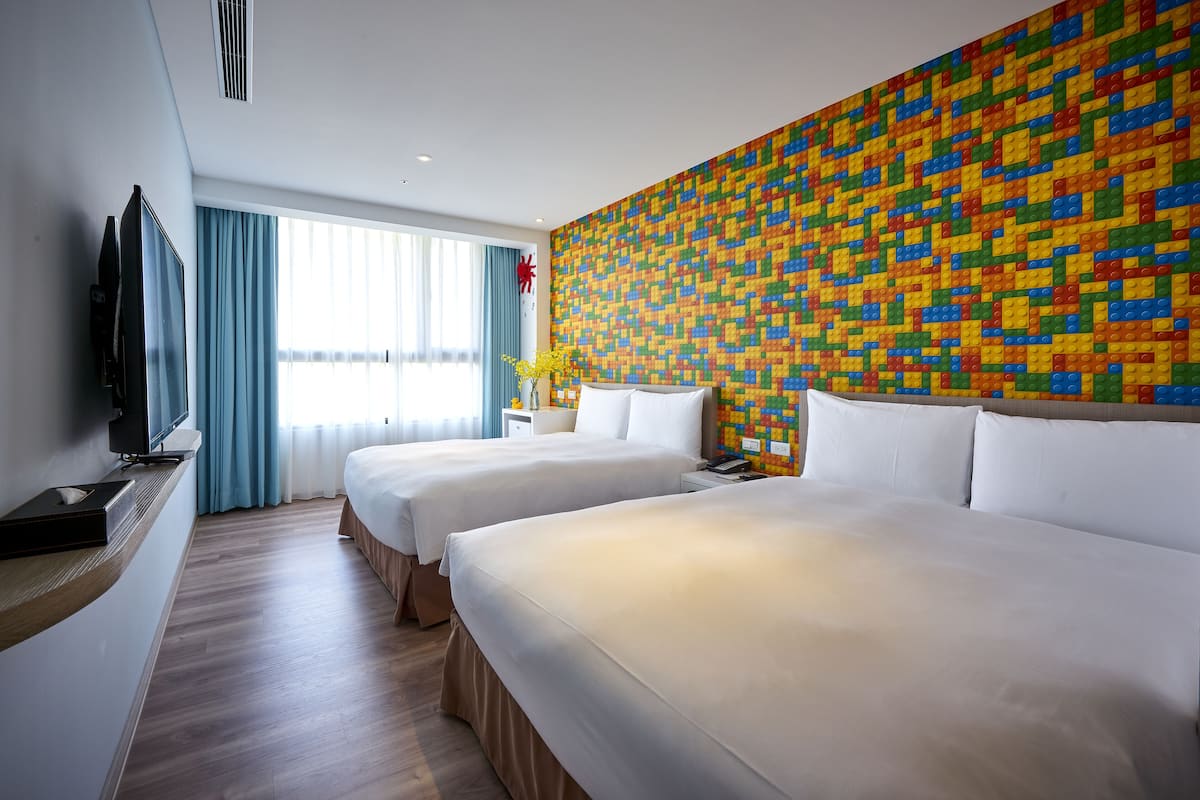 A hotel room with two beds, a TV, a window with curtains, and a colorful wall.