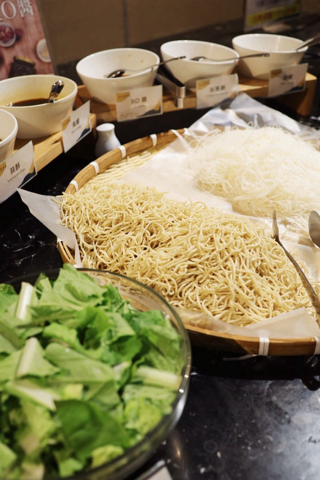 A buffet setup with various food items including noodles, vegetables, and bowls.