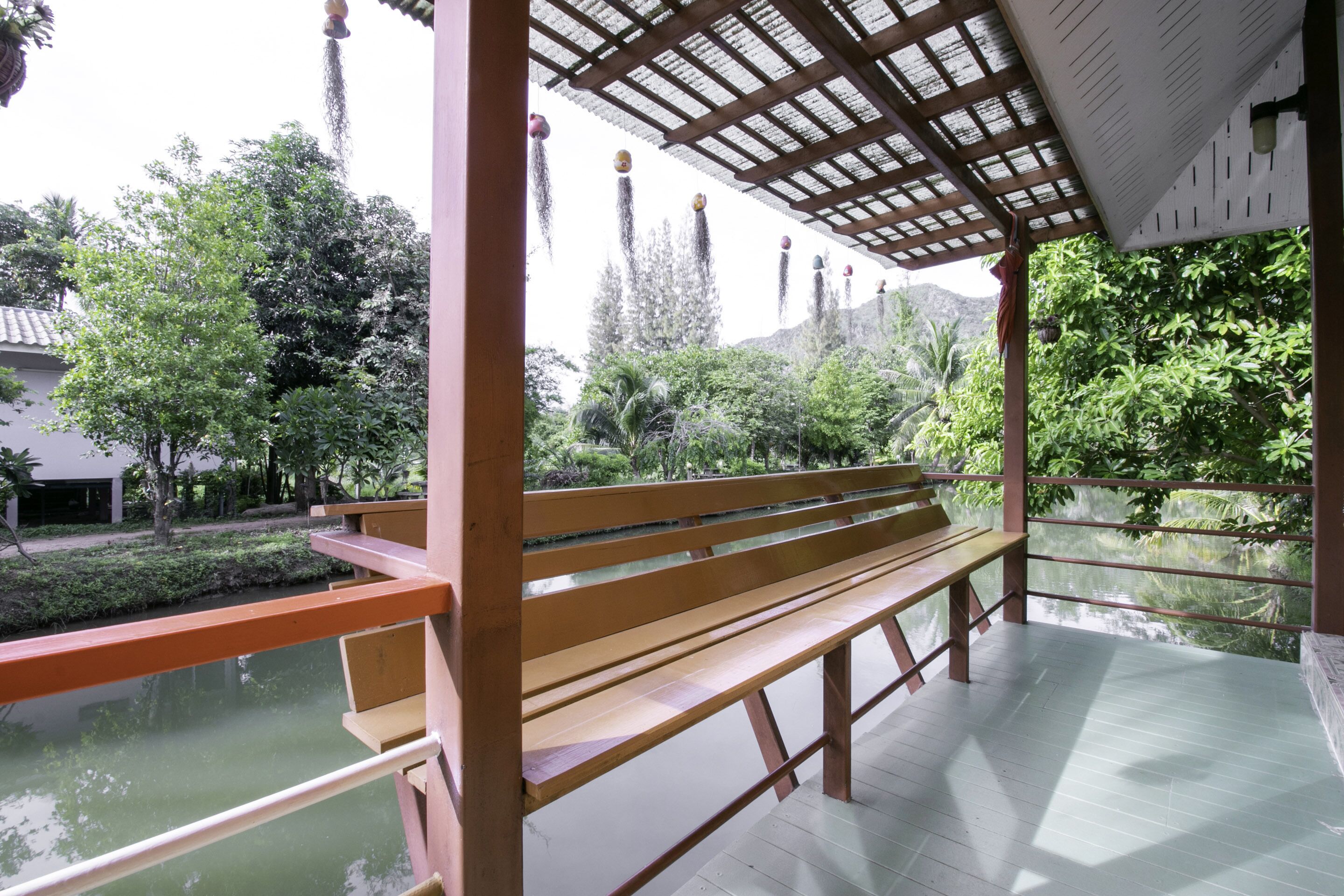 A wooden bench under a pergola with a view of a water body and greenery.