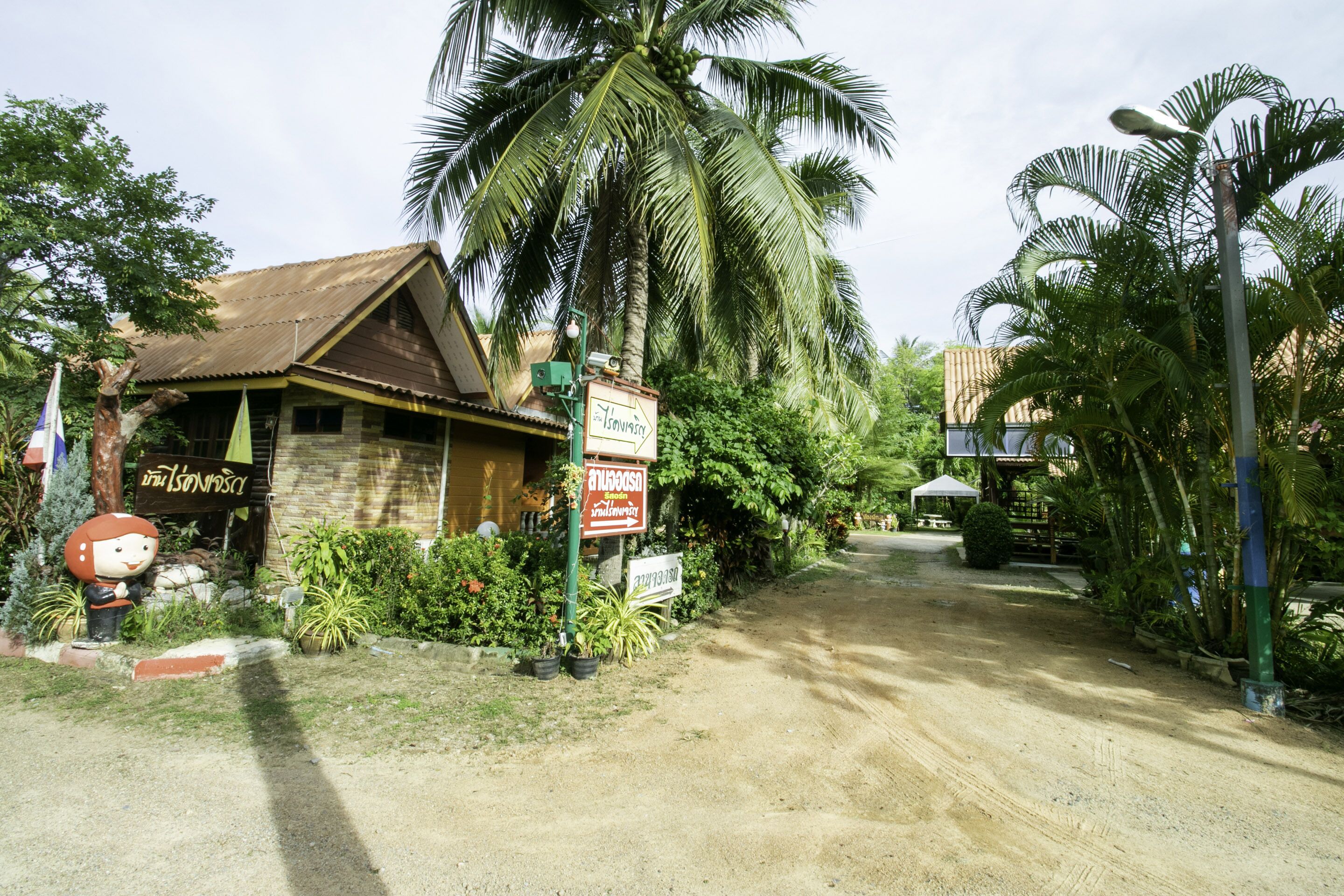 A rustic building with a signboard, surrounded by lush greenery and palm trees.