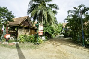 A rustic building with a signboard, surrounded by lush greenery and palm trees. - OYO 1062 Baanrai Kongjaroen (Cha-am)