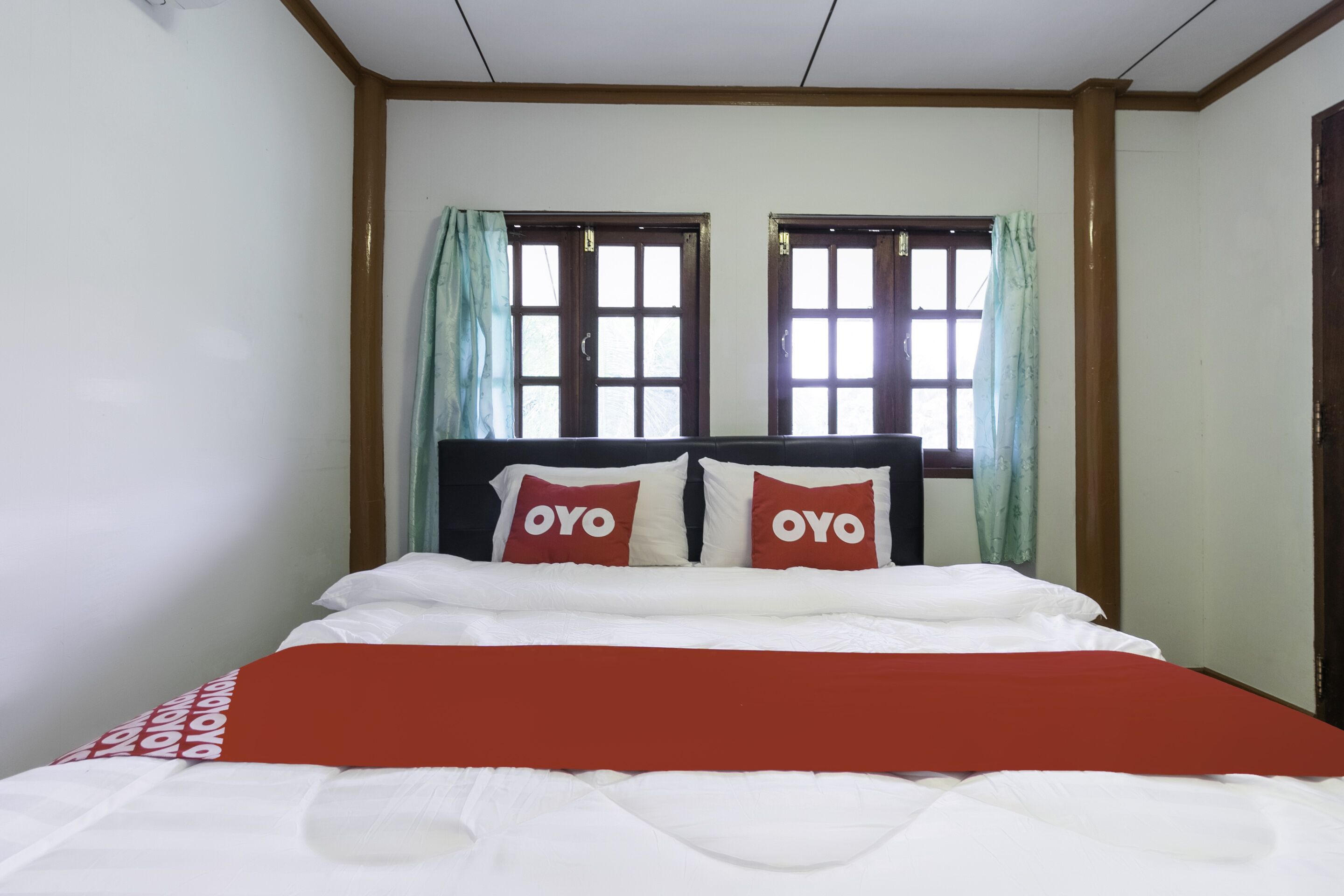 A hotel room with a bed, two windows with curtains, and a wooden headboard.