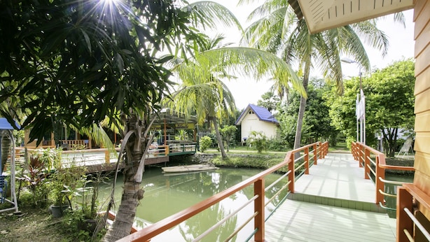 A wooden bridge over a calm water body, surrounded by lush greenery and palm trees. - OYO 1062 Baanrai Kongjaroen (Cha-am)