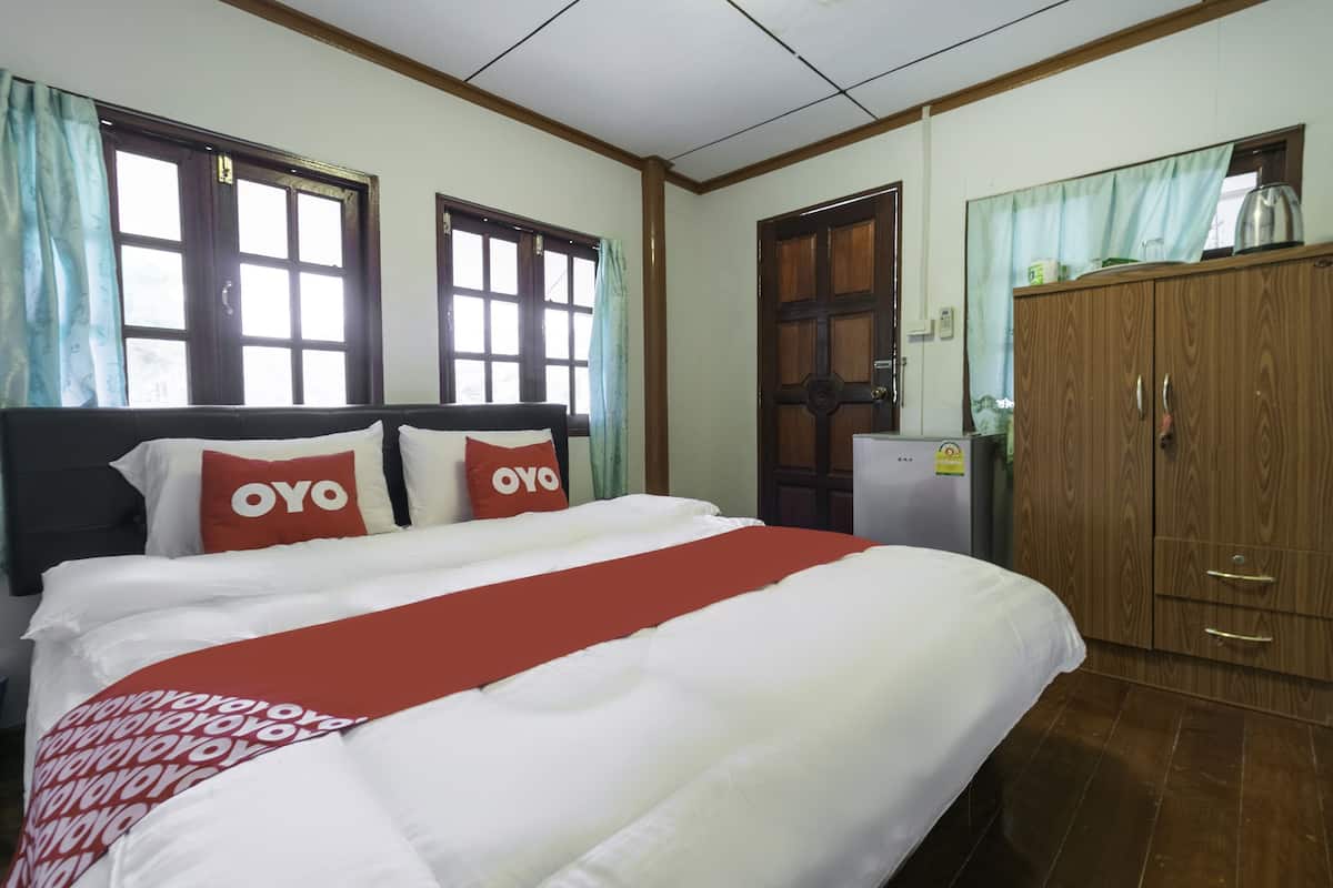 Ett hotellrum med en säng, två kuddar med ordet "OYO", en garderob i trä och ett fönster med gardiner.
