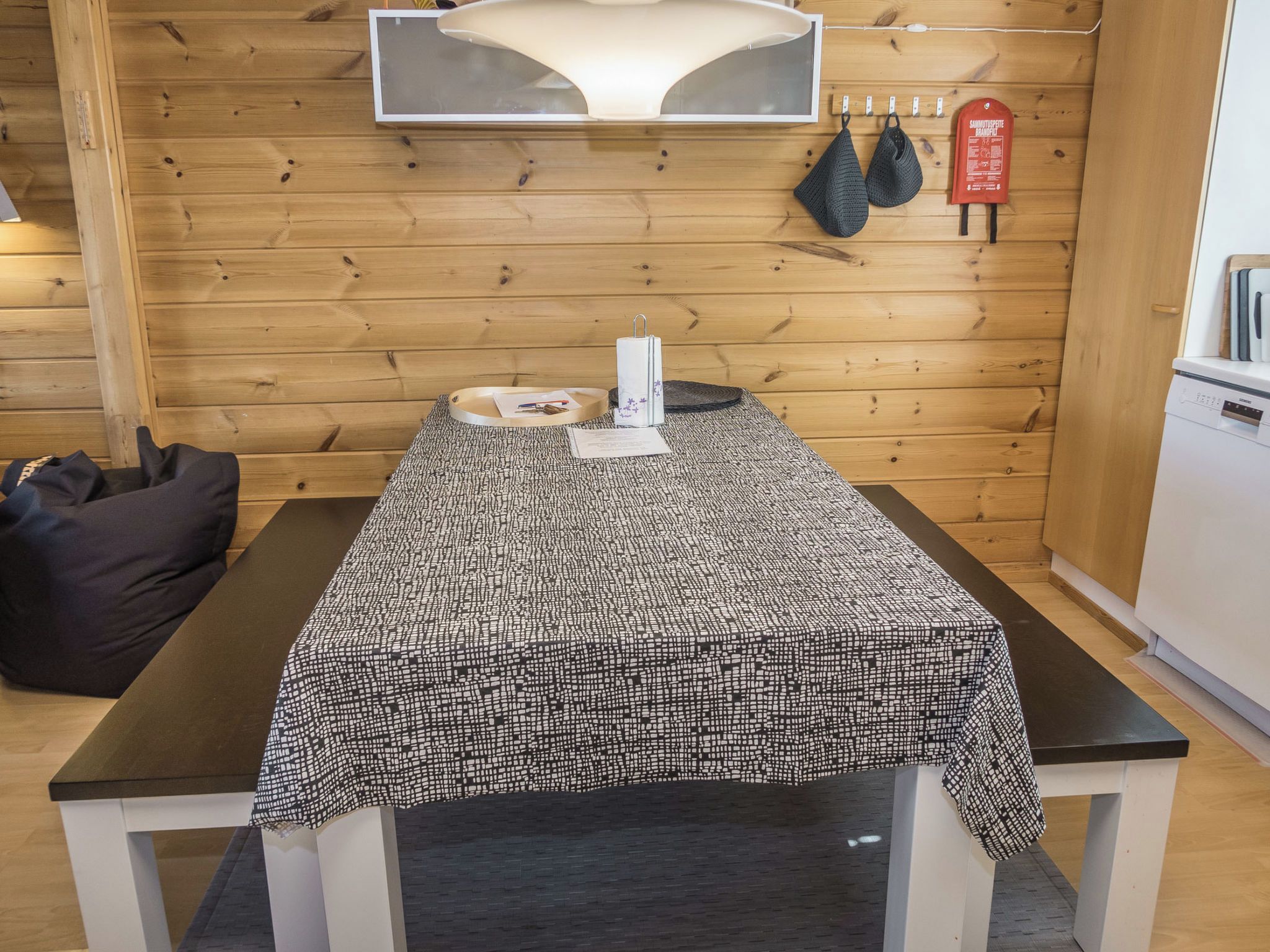 A wooden interior with a table covered by a patterned tablecloth, a black bag, and a white appliance.