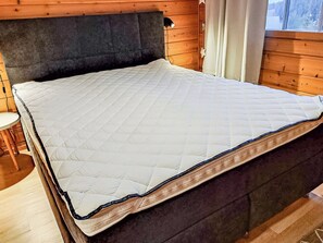 A bed with a quilted mattress in a room with wooden walls and a window. - Rukan komia chalet by Interhome (Kuusamo)