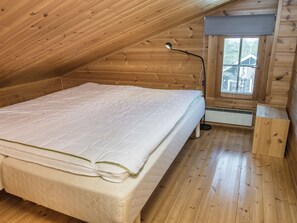 A single-bed room with a sloped ceiling, wooden walls, a window with a view, and a bedside lamp. - Rukan komia chalet by Interhome (Kuusamo)