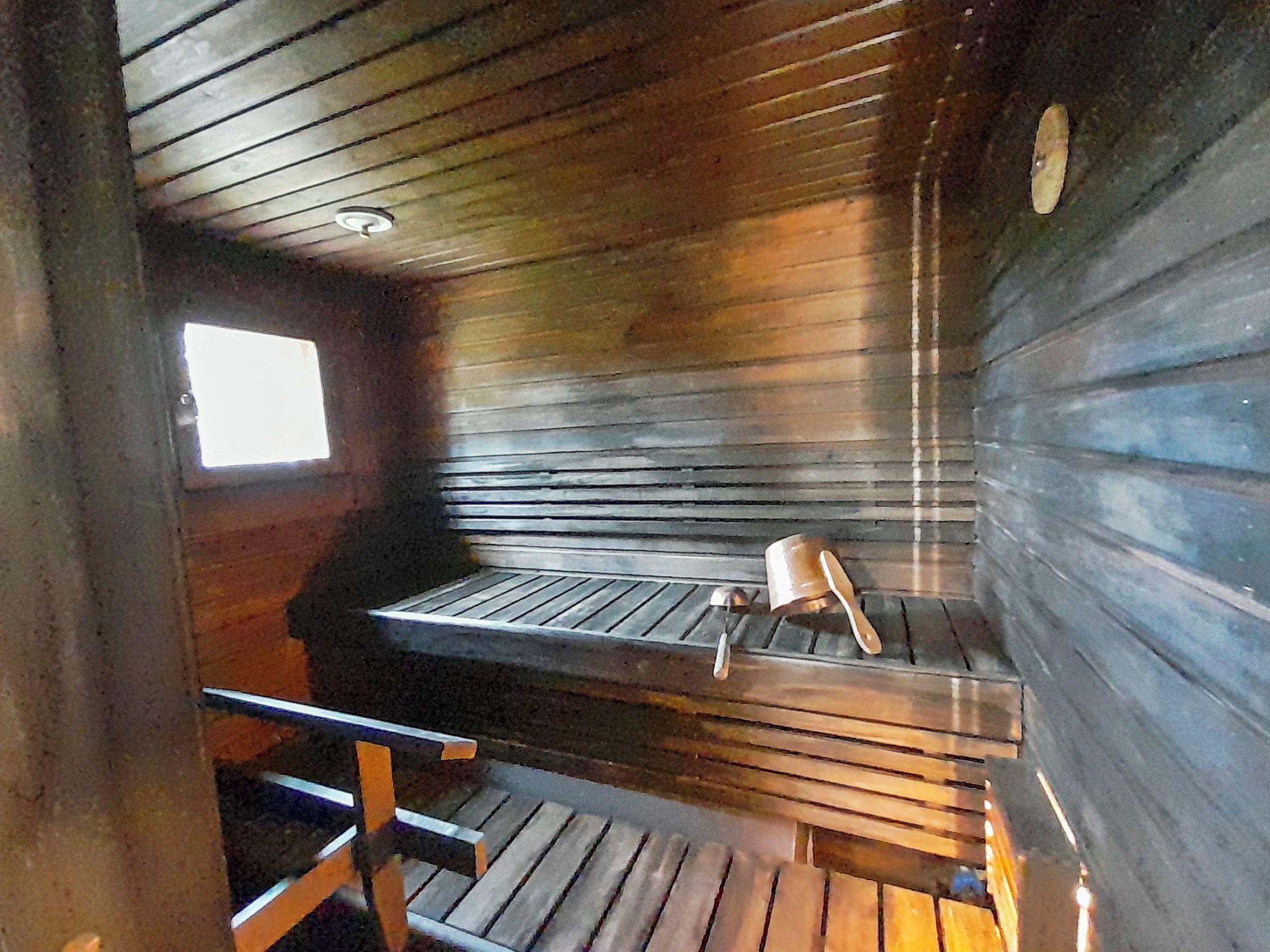 L'intérieur d'une cabane avec un banc en bois, une fenêtre et une rambarde en métal.