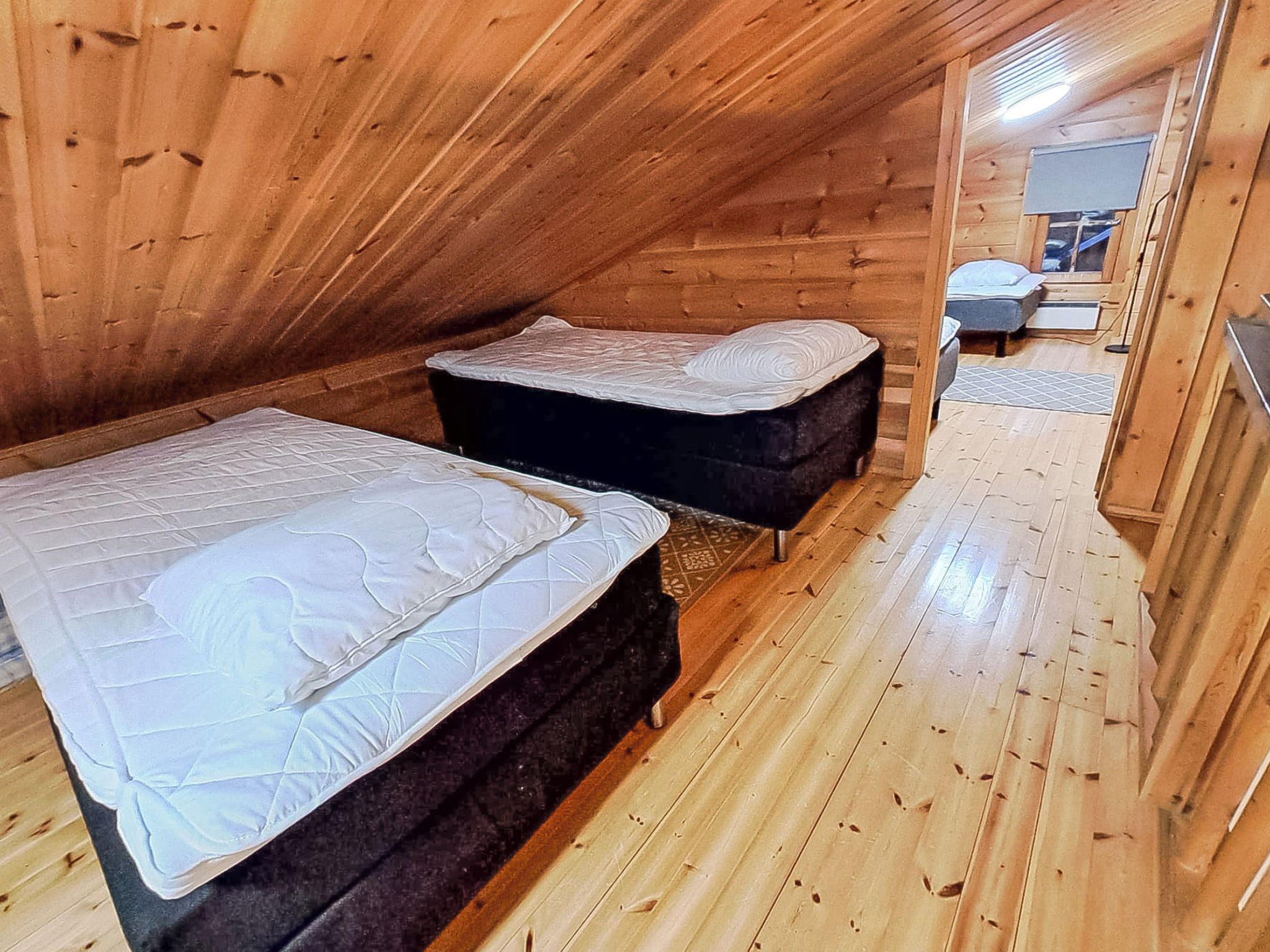 A small, wooden attic bedroom with two beds and a bench.