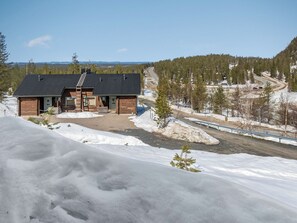 A cabin with a wooden exterior, a black roof, and a front porch. There is a clear view of a snowy landscape and a road in the background. - Rukan komia chalet by Interhome (Kuusamo)
