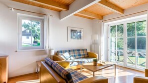 Ein modernes Wohnzimmer mit Holzboden, großen Fenstern, einer Couch und einem Couchtisch.