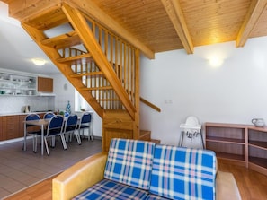 A cozy interior with a wooden staircase, a dining area with blue chairs, and a sofa with a plaid cushion.