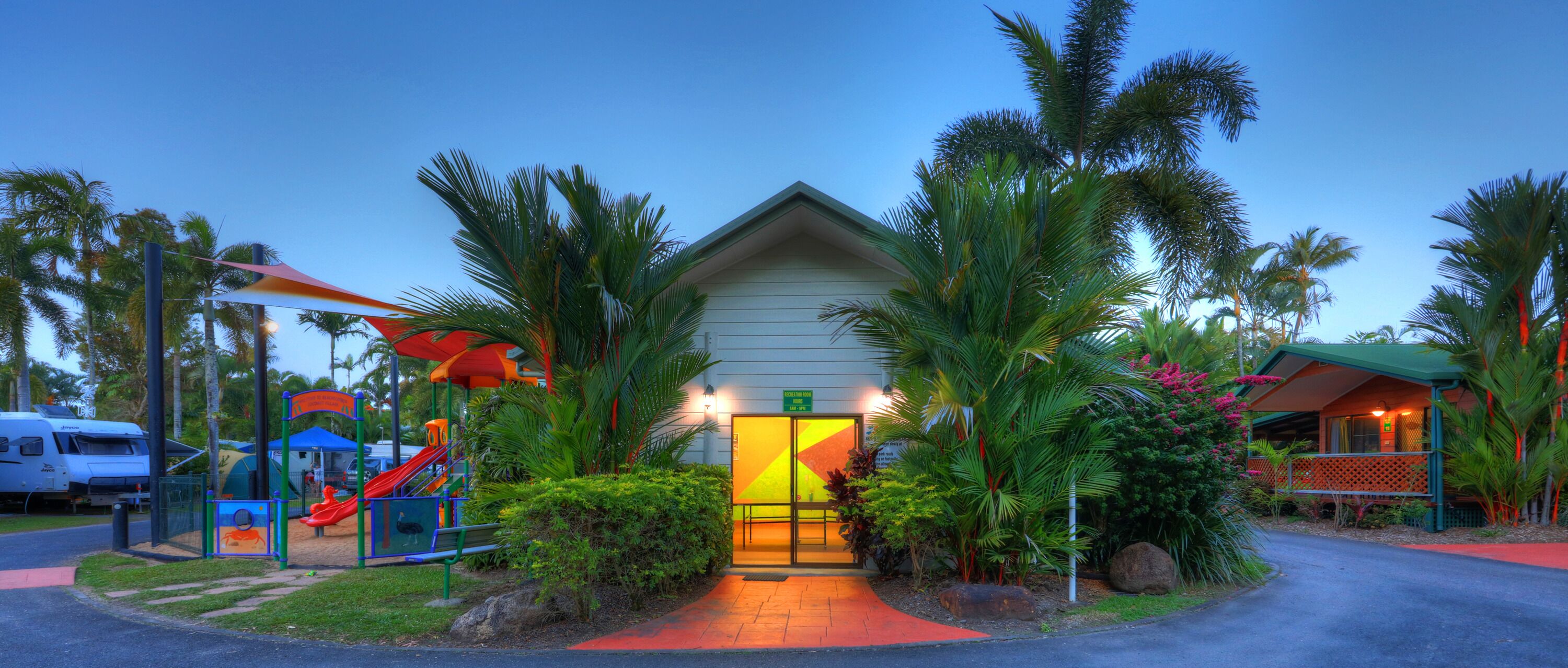 A hotel entrance with a play area, palm trees, and a clear sky.