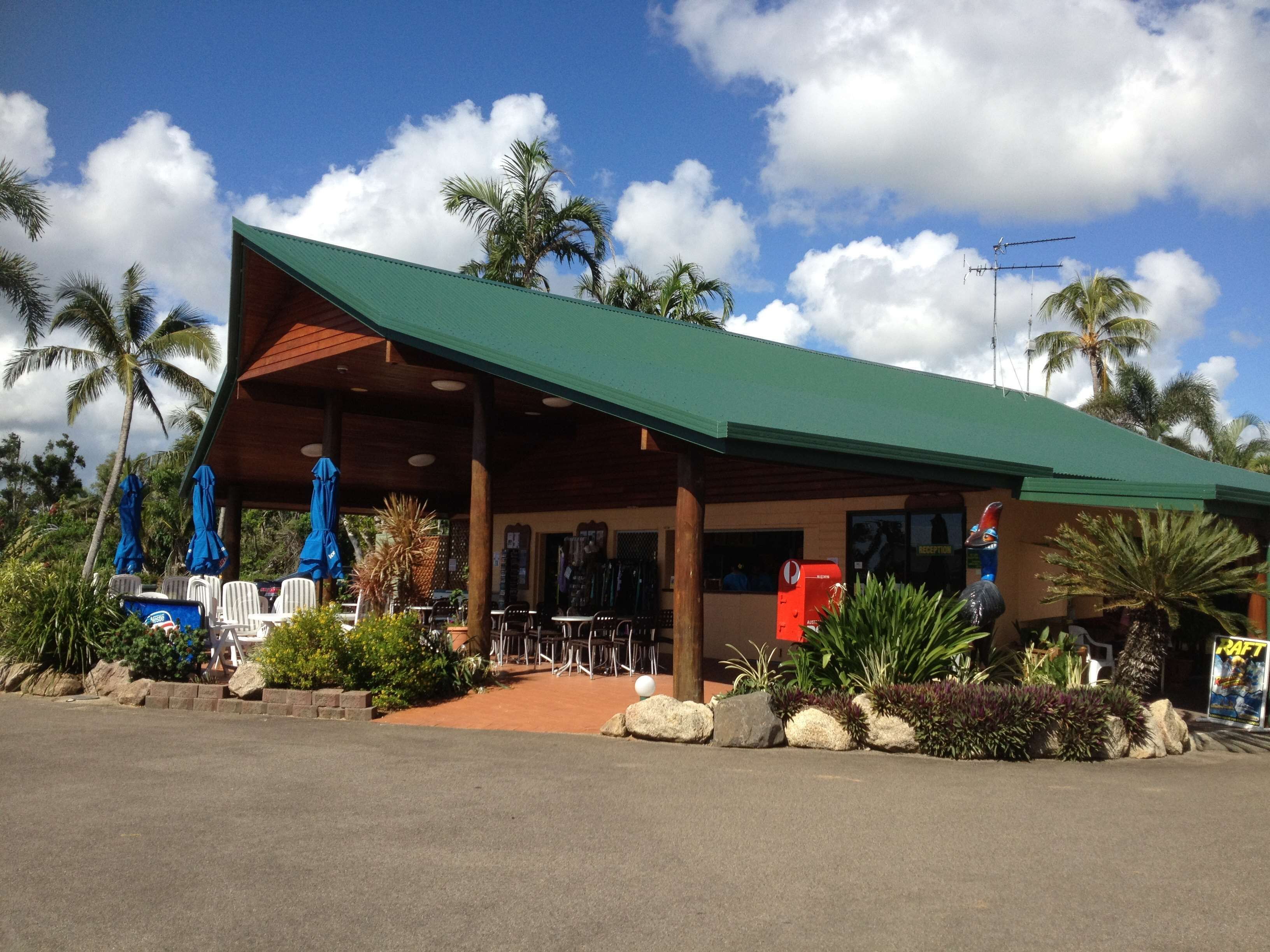 A building with a green roof, outdoor seating, and palm trees.