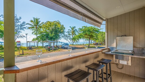 Zona de bar con taburetes y vista a la playa y palmeras.