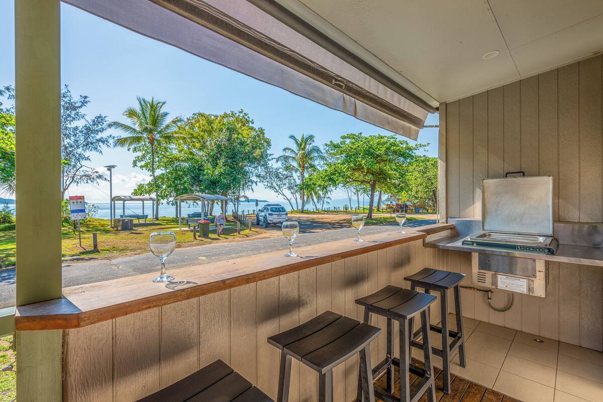Un espace bar avec des tabourets et une vue sur la plage et les palmiers.