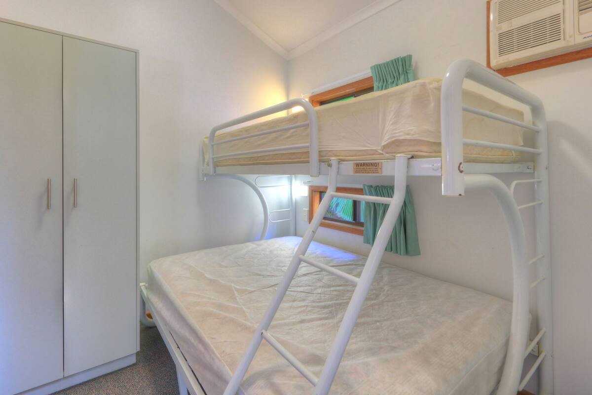 Un lit superposé avec une échelle, une armoire et une fenêtre avec des rideaux.