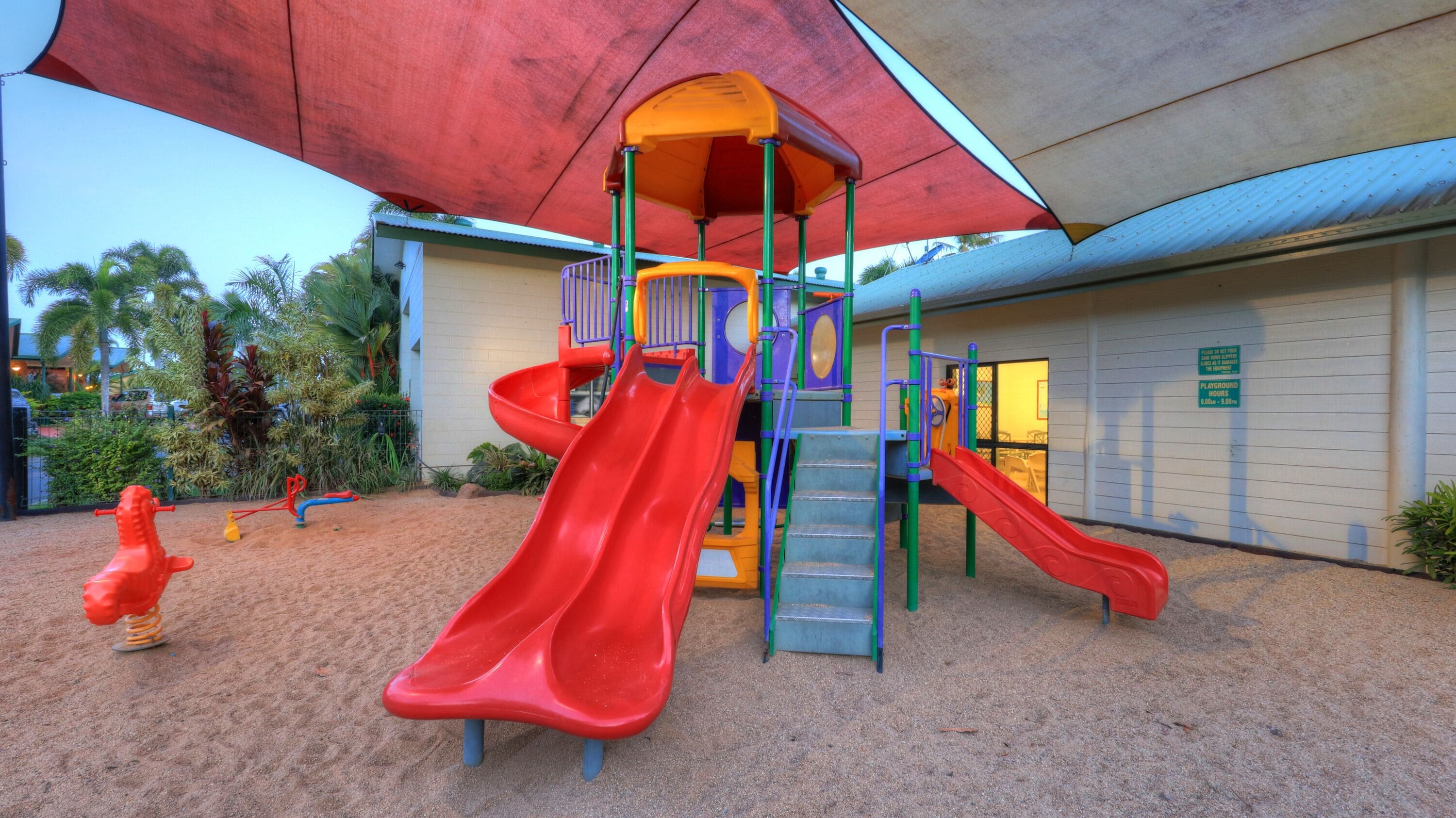 Une aire de jeux avec deux toboggans rouges, une structure d’escalade et un espace abrité.