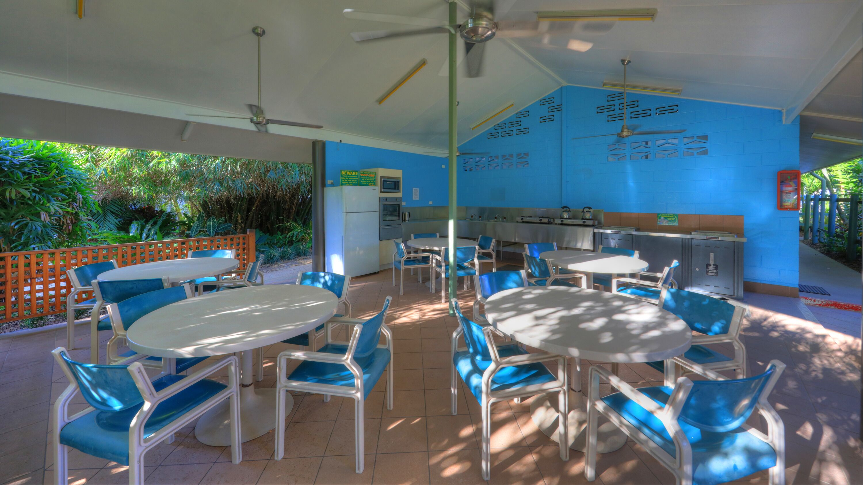 Un espacio al aire libre techado con mesas y sillas, una zona de cocina y vistas a la vegetación.