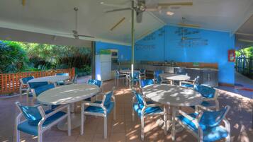 Un espacio al aire libre techado con mesas y sillas, una zona de cocina y vistas a la vegetación.
