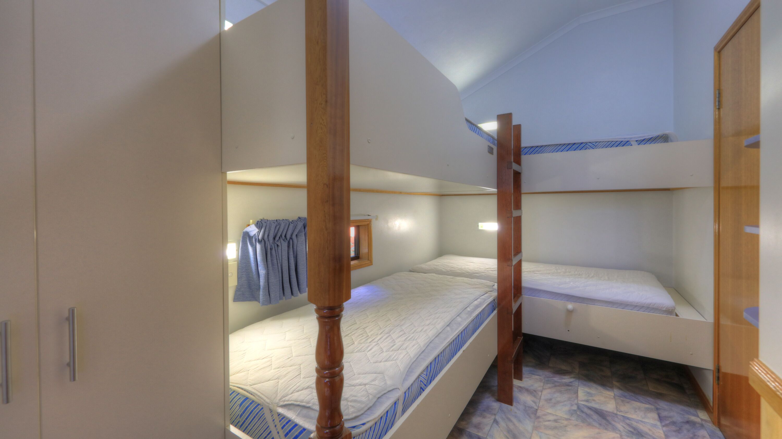 A dormitory-style room with bunk beds, wooden furniture, and a tiled floor.