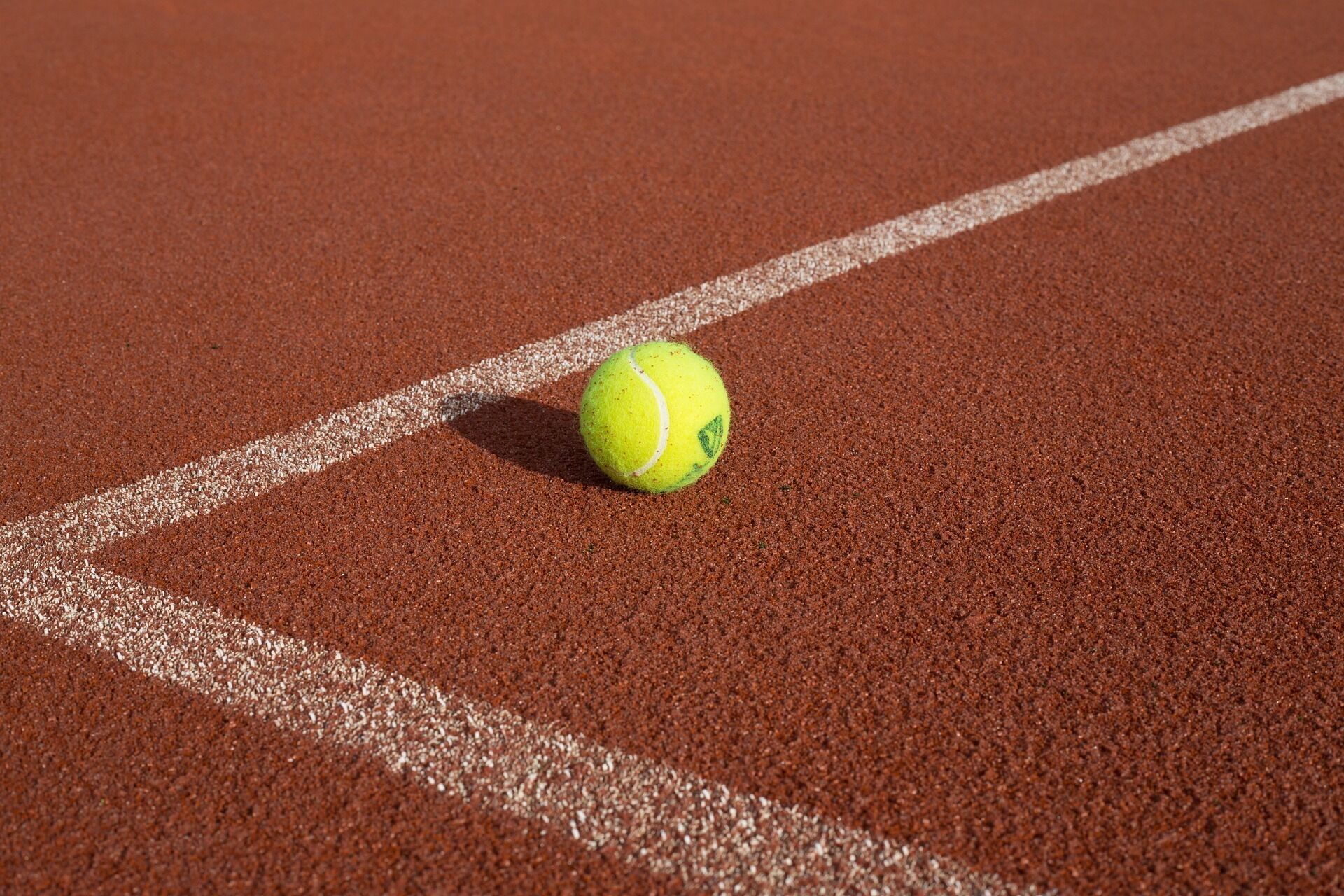 A tennis ball on a red clay court with white boundary lines.
