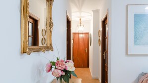 Un pasillo con un espejo, un jarrón de flores y una puerta al final.