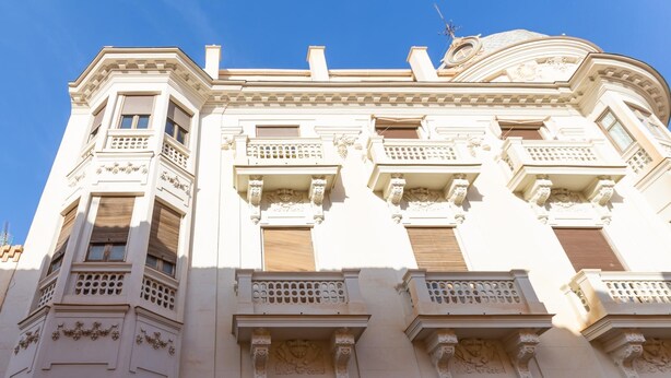 Un edificio de varios pisos con detalles arquitectónicos ornamentados, incluyendo balcones y molduras decorativas.