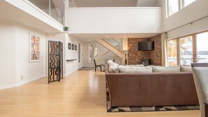 Amplia sala de estar con techo alto, chimenea de piedra, televisor de pantalla plana y un ventanal con vistas al exterior.