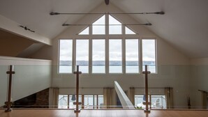 Una habitación amplia con un tragaluz grande, piso de madera y vistas a un cuerpo de agua y colinas distantes.