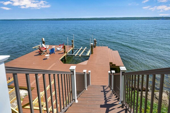 A wooden dock with a metal railing, a small boat, and a row of chairs and tables.