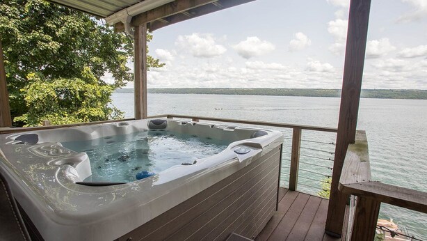 Jacuzzi en una terraza de madera con vista a un lago y árboles.