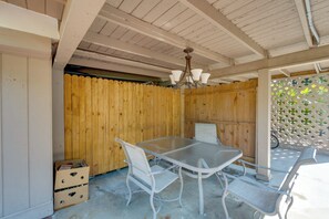 Un patio cubierto con una mesa y sillas, paredes de madera y techo con vigas a la vista.