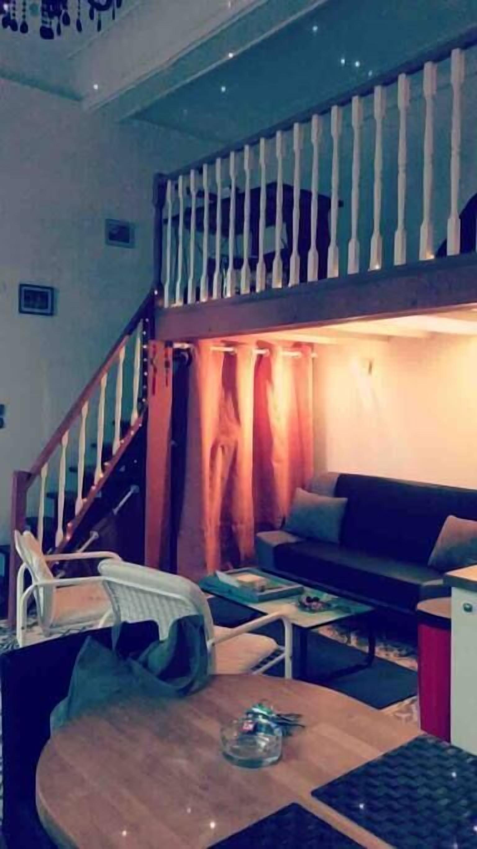 A room with a bunk bed, a staircase, a sofa, and a small table.