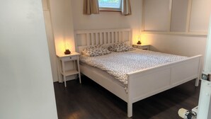 A bedroom with a white bed, floral bedding, two bedside lamps, and a window with curtains.