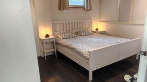 A bedroom with a white bed, floral bedding, two bedside lamps, and a window with curtains.