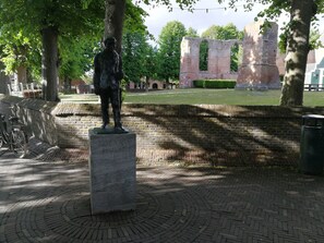 Uma estátua de um homem sobre um pedestal em um parque com caminhos e muro de tijolos.